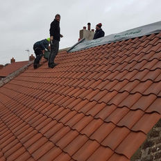 Roofers installing red pantile tiles on a pitched roof slope