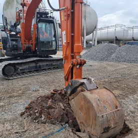 Orange excavator digging soil at construction site with gravel, tanks