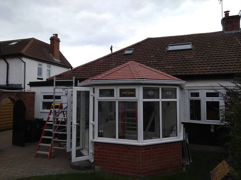 A newly constructed brick conservatory with large windows and a red tile roof is attached to a house