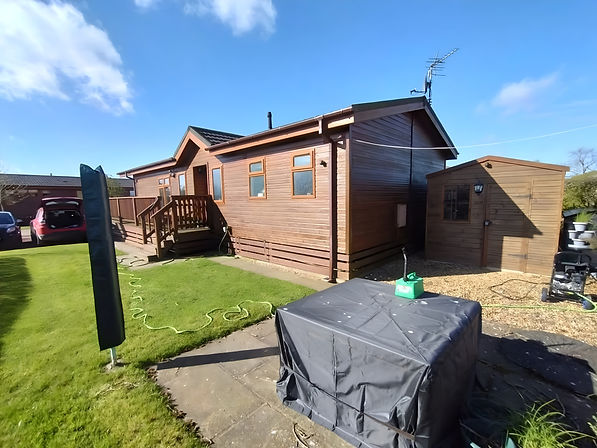 Exterior of a timber park home with an attached shed and wooden steps leading to the entrance