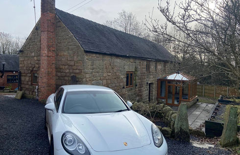 White sports car parked in front of a rustic stone house with a chimney