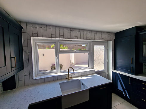 Modern kitchen with natural light, featuring a large window, dark blue cabinets