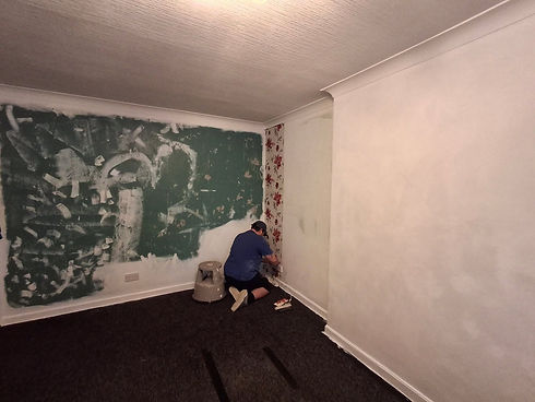 Tradesperson kneeling on the floor, applying floral wallpaper to a room undergoing renovation