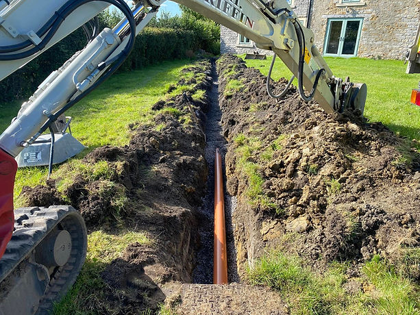 Close up of an orange drainage pipe laid in a freshly dug soil trench on a site