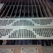 Perforated semi-circular metal baffle plates resting on a laser cutting bed slat table inside a fabrication shop