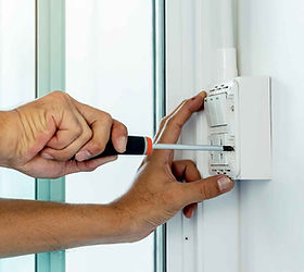 A person uses a screwdriver to adjust a white thermostat on a wall