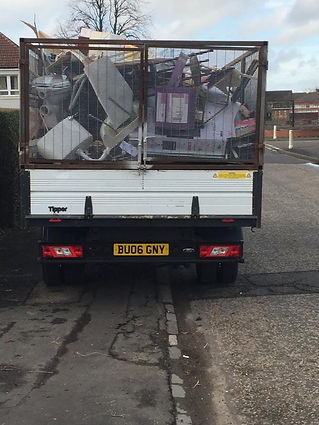 A truck loaded with a jumble of appliances and debris in a cage, parked on a suburban street