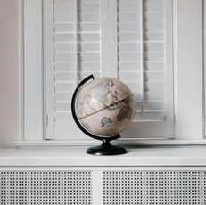 Decorative globe on a window sill in front of closed white plantation shutters
