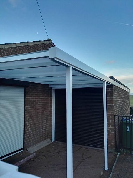 A modern white canopy with clean lines attached to a brick building, covering a paved area