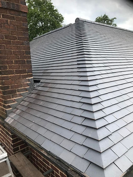 Close-up of a newly completed grey tile roof layout with lead flashing detail against a brick wall