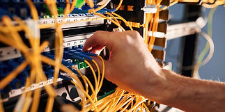 A hand adjusts blue cables among orange wires in a server rack