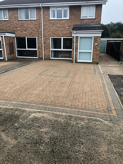 Block paved driveway in front of a brick residential property with white window frames