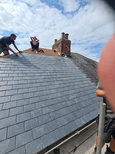 Roofers carrying out timber batten repairs on a slate roof next to a chimney stack