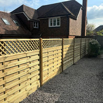 A wooden fence with lattice top runs along a gravel pathway beside a brick house with gabled roof