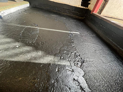 Black waterproof tanking membrane applied to an internal brick wall and floor section during damp treatment