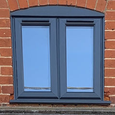 Arched window with blue glass and gray frame set in a red brick wall, reflecting a clear sky
