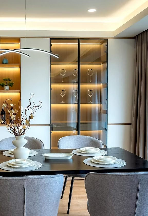 Ein Esszimmer mit aufgedecktem Geschirr. Dahinter ein Einbauschrank mit Glasfronten und darin platziertem Geschirr.