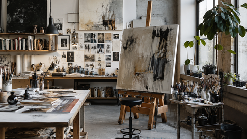 Ateliê de pintura com telas abstratas no cavalete, mesa cheia de pincéis, plantas na janela e luz natural suave.