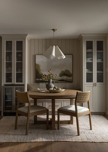 Warm Waterloo dining room with round wood table, sculptural pendant, custom fluted-glass cabinetry and landscape artwork