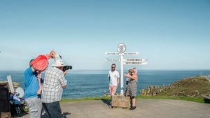 Een beroepsfotograaf maakt een foto van toeristen bij de iconische richtingaanwijzer op de klif van Land's End. Fine art fotografie van Leon Bouwman, serie Photo. | A professional photographer taking a photo of tourists at the iconic Land's End signpost on the cliff. Fine art photography by Leon Bouwman, series Photo.