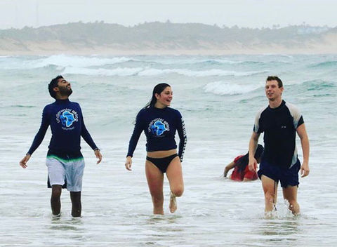 Three people exit the water on the beach and laugh