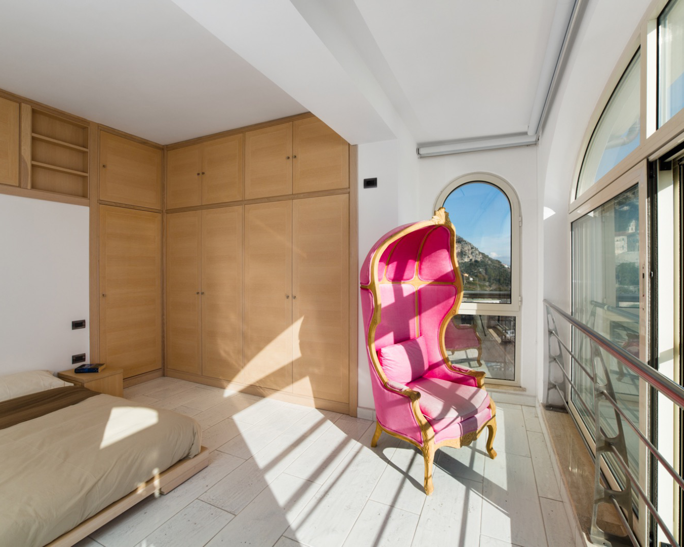 Bedroom with pink chair, cabinets, and arched window. Home design studio services PHASEZERO DESIGN