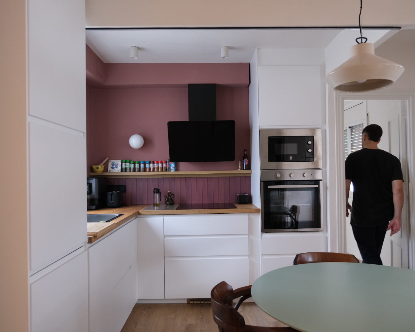 Modern kitchen with white cabinets, appliances, and a person walking towards the room.