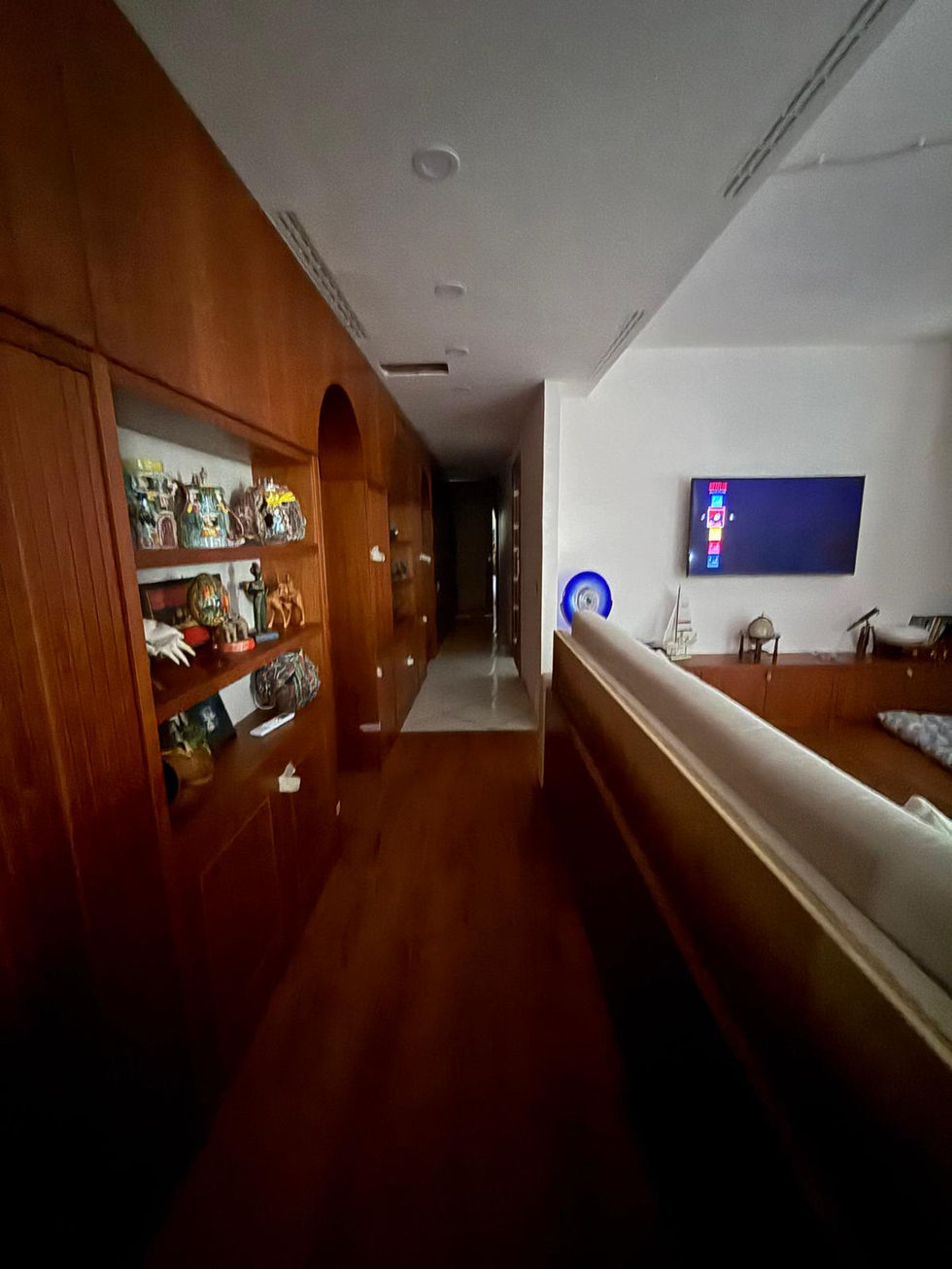 Long hallway with wooden shelves and living room