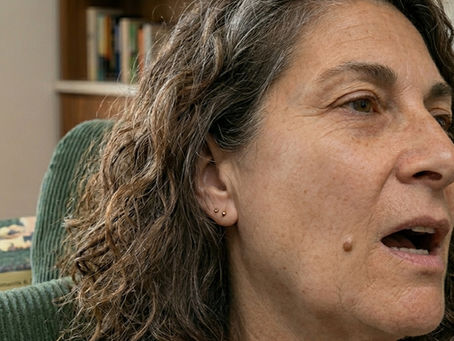 Primer plano de una mujer con problema mandibular en un sillón verde; detrás se ve un libro Cien años de soledad en un salón cálido.