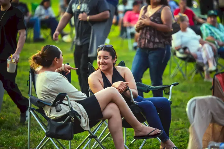 Amigas conversando mientras disfrutan del concierto al aire libre en Stone Park