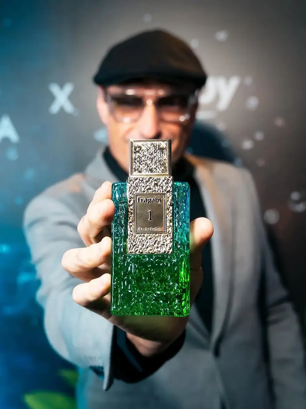 Retrato de hombre con traje y gafas sosteniendo el frasco de Fragaby Perfume verde con detalles dorados, resaltando la exclus