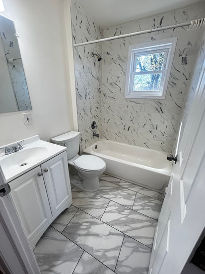Renovated bathroom with marble-style tile walls, modern vanity, and bathtub
