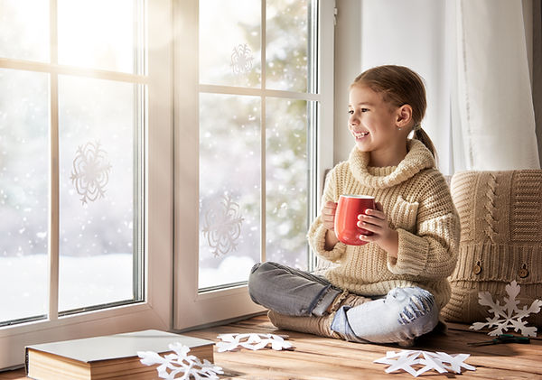 Young girl drinking hot chocolate while looking out snowy window — peace of mind from reliable snow removal services