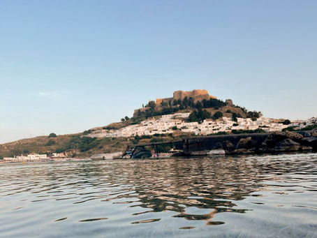 View of Lindos Acropolis and whitewashed houses from the sea, representing the destination featured in the Lindos parking guide.