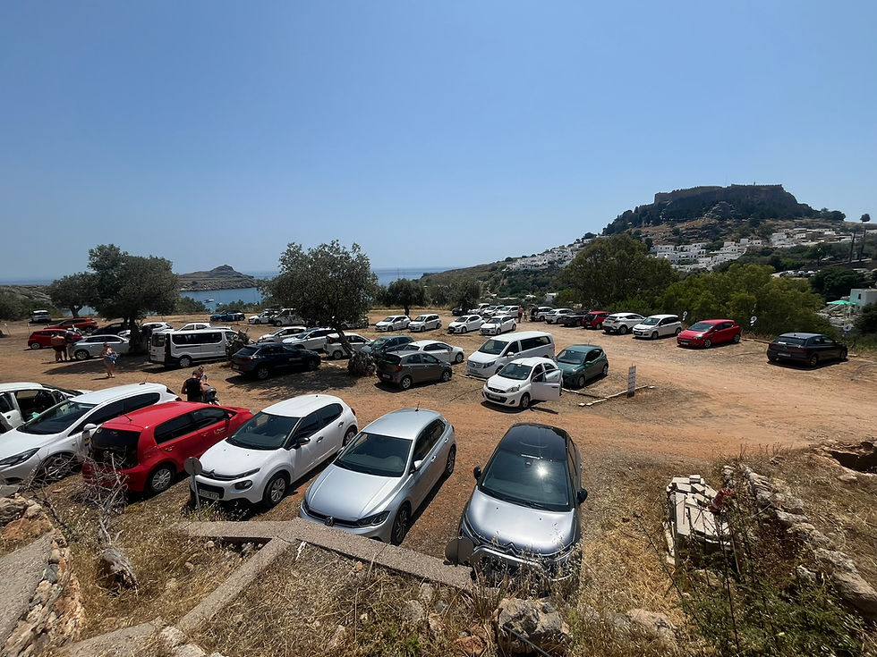 Lindos Heart Parking lot near Lindos Beach and the village center, showing shaded and organized parking area with sea view in the background.