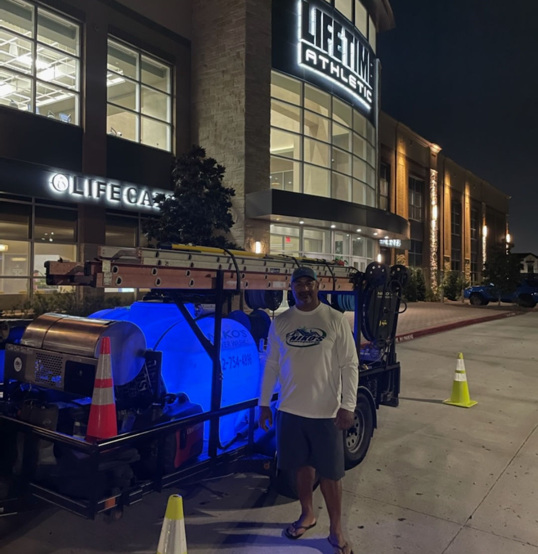 Niko, owner of Niko's Power Washing, standing next to a blue cargo bike in front of Lifetime Athletics building at night