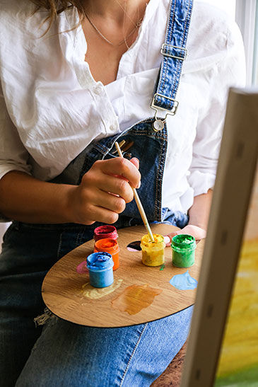 woman with painting hobby dips her paint into a small jar of yellow
