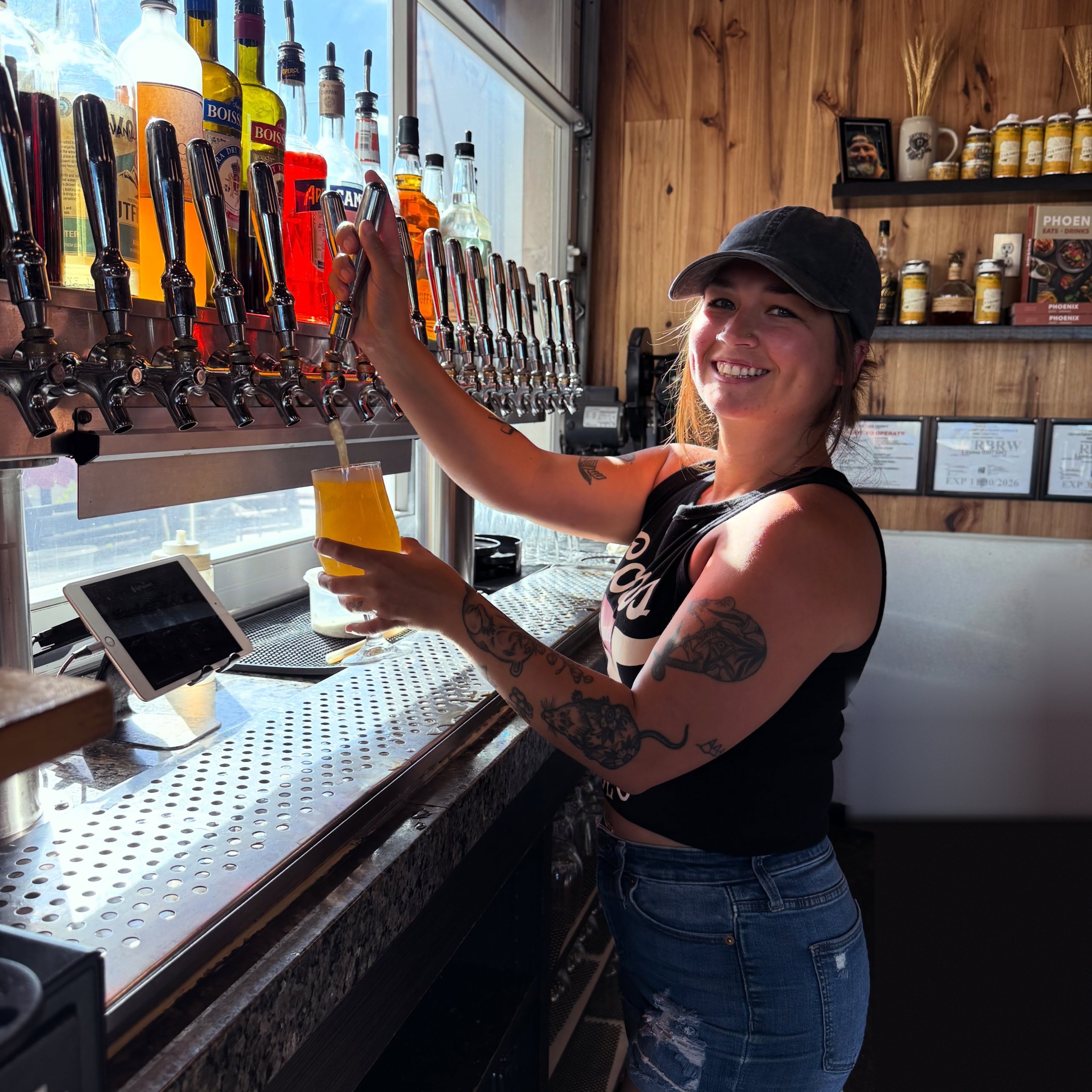 A bartender pouring a house beer at the tap wall inside Peoria Artisan Brewery