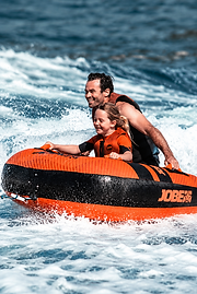 Two people riding an orange towable tube on the water
