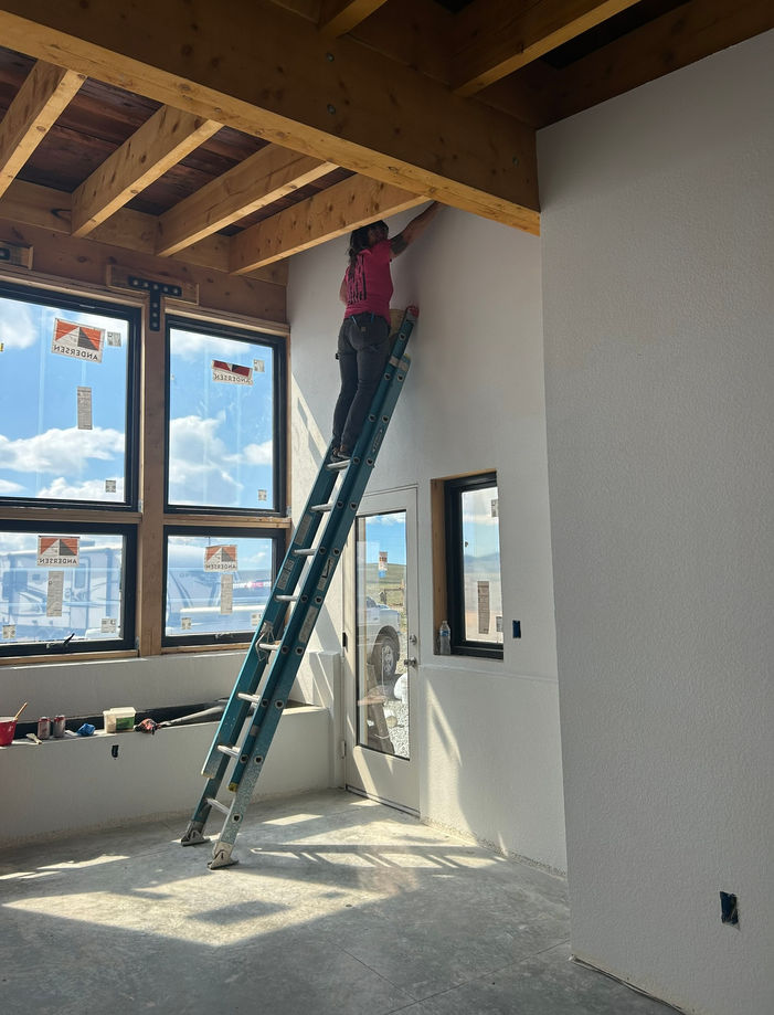 Woman standing on extension ladder inside office space, cleaning the ceiling.