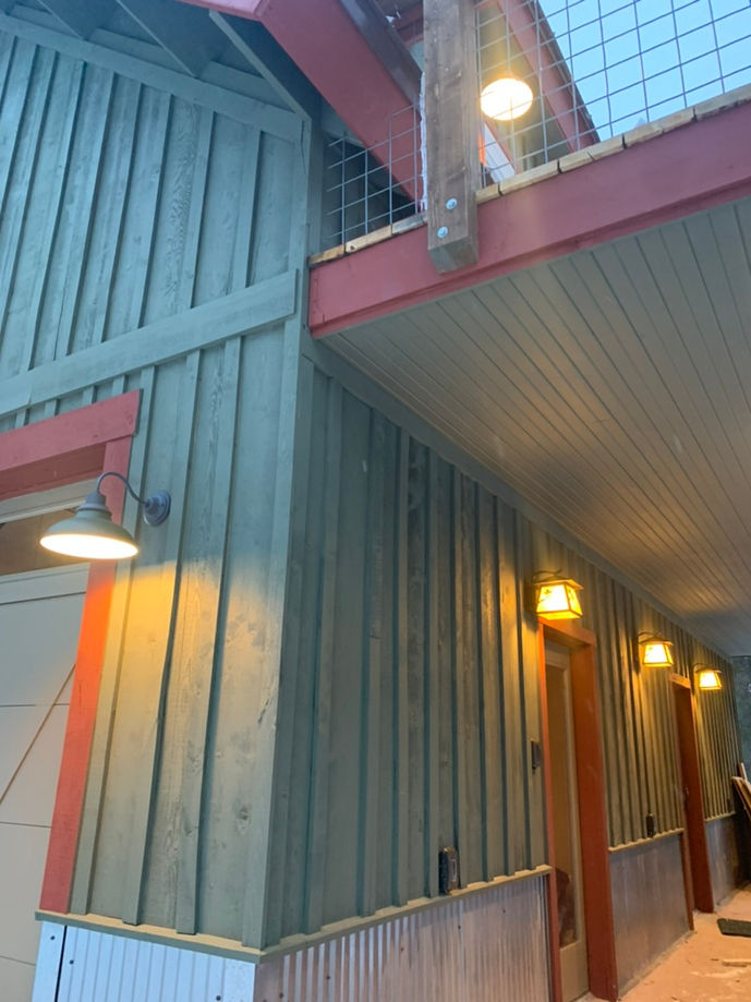 Corner shot of board and batten exterior. Exterior is painted dark sage green with burnt red trim. Heave timber is exposed in the second floor porch