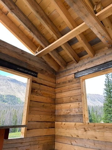 Picture of interior of partially built log cabin with large mountains framed in the window bays.