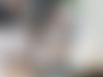 Woman wearing a light blue hijab clapping and smiling at a laptop. Office setting, neutral tones, shelves in background.