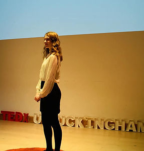 Grace Spicer on the TEDx Stage wearing a white blouse and black pencil skirt.