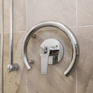 A close-up of a circular grab bar installed around a shower control handle in a bathroom.