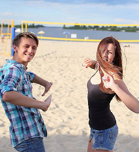 Two young people dancing on the beach. They look somewhat awkward, but are smiling and having fun anyway.
