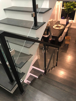 Modern staircase with glass railing and dining area.