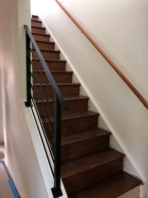 Wooden staircase with black railing and white walls.