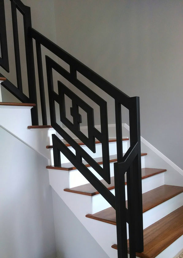 Black geometric railing on wooden staircase.