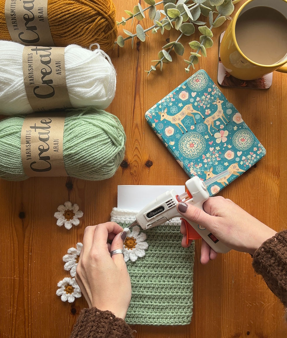 Female hands using a glue gun to attach crochet daisy applique to a crochet kindle sleeve